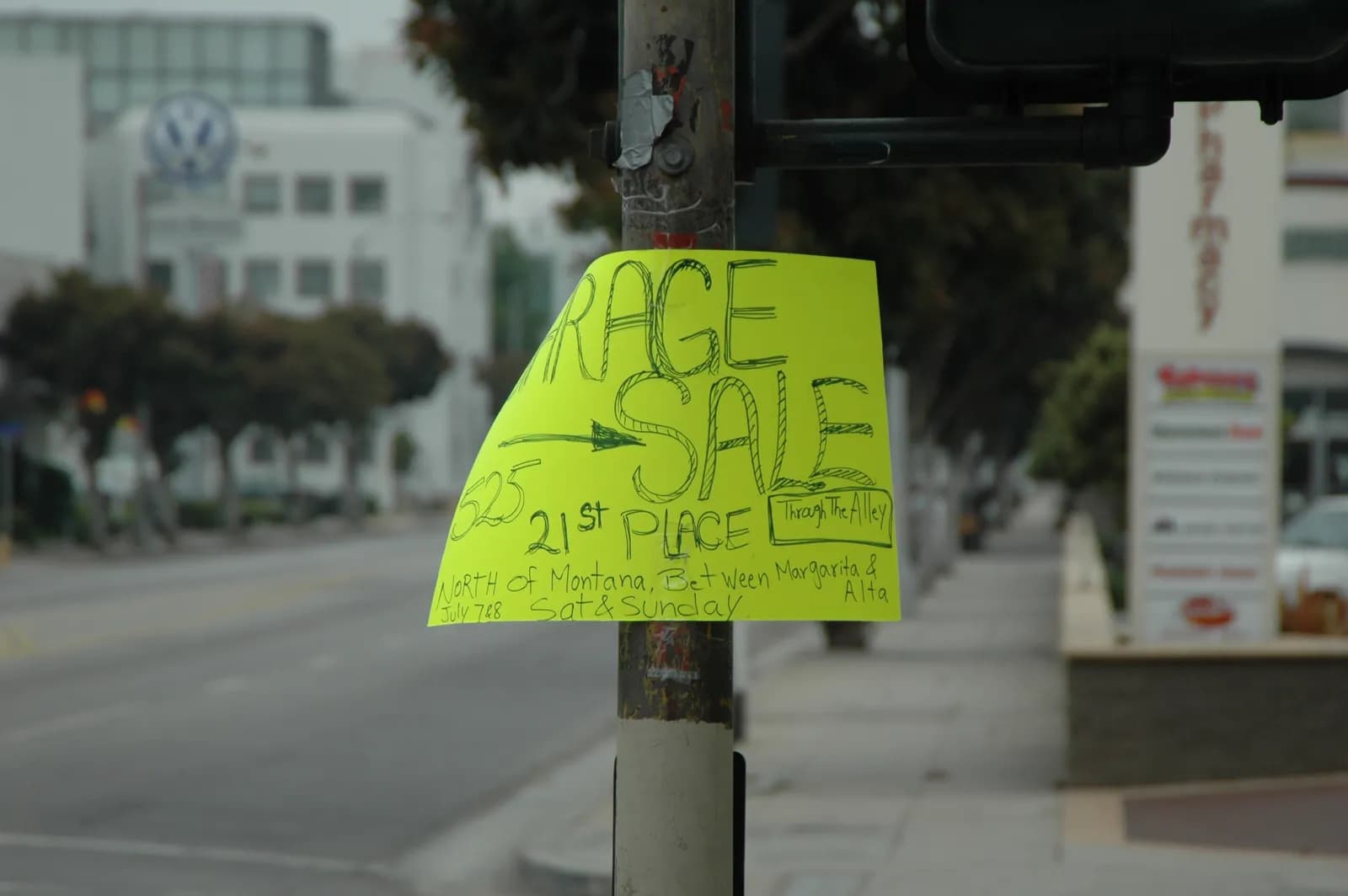 A fluorescent yellow hand-drawn Garage Sale sign taped to a street-light pole on a commercial street, with an address on 21st Place.